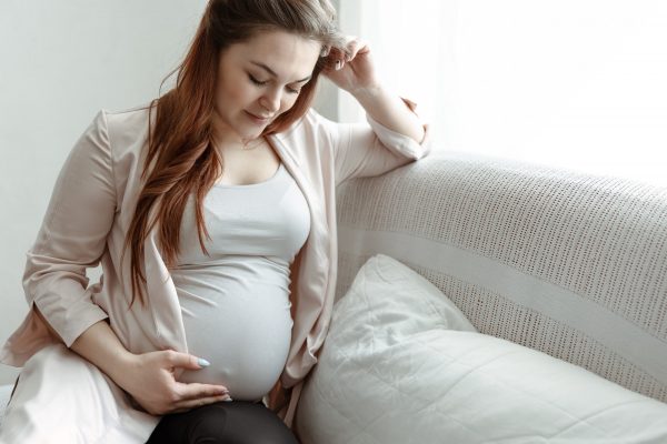 Young pregnant woman is sitting on the sofa at home.