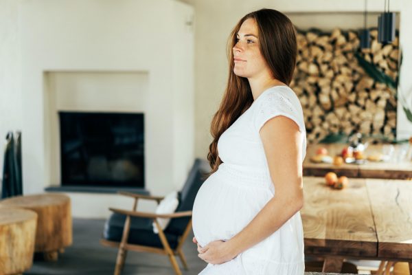 A pregnant woman in a white dress hugs her stomach with her hands. Waiting for the birth of a baby